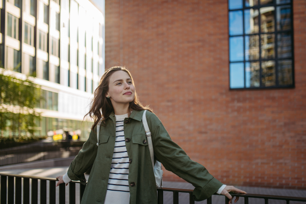 Portrait of a young woman in a city, standing in front red brick building.