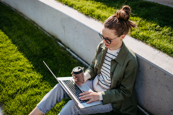 Young woman sitting in city park and working on a laptop.