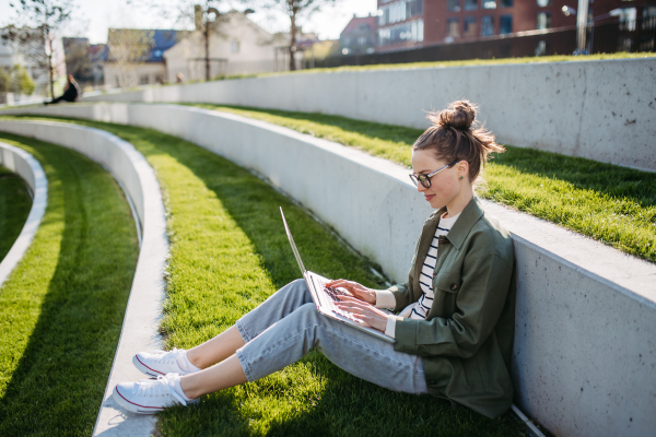 Young woman sitting in city park and working on a laptop.