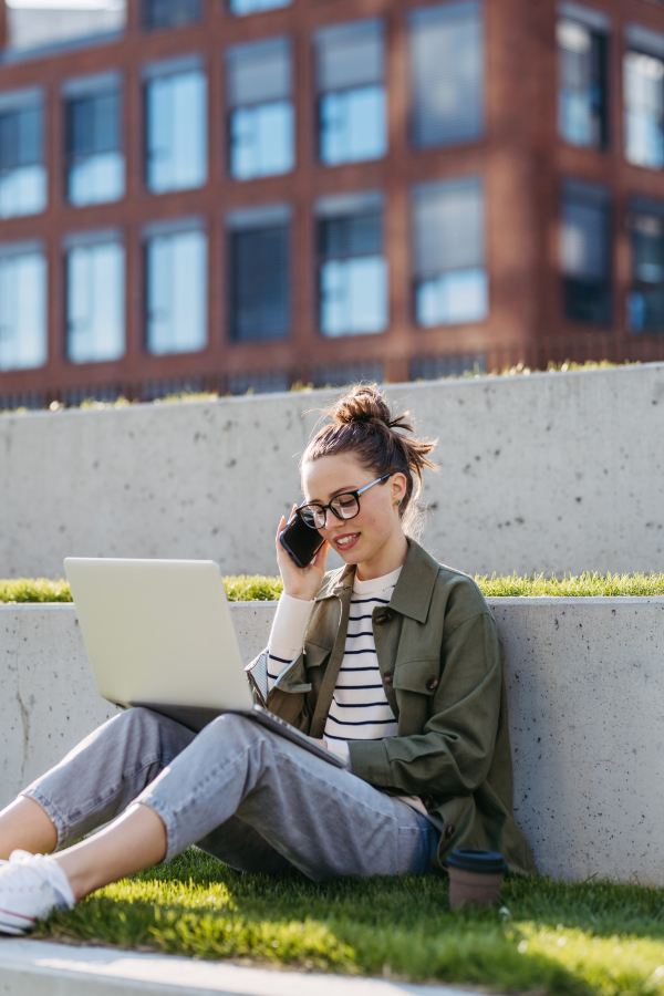 Young woman sitting in city park and working on a laptop.