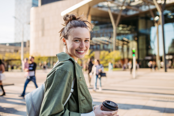 Portrait of young woman wearing glasses on city street, standing in front red brick building.