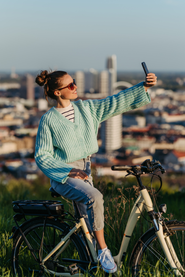 Young woman on an electro bicycle, taking selfie concept of commuting and ecologic traveling.