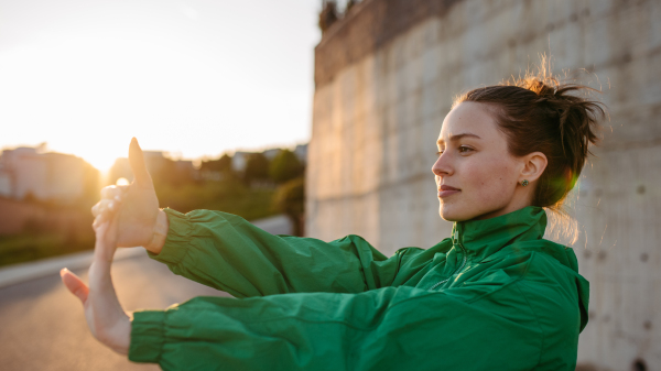 Yung woman in sportive clothes doing stretching in a city.