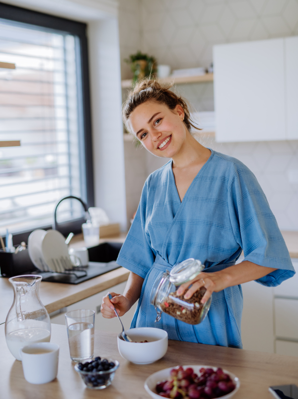 Young woman preparing a muesli for breakfast in her kitchen, morning routine and healthy lifestyle concept.