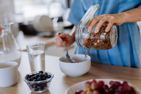 Close-up of young woman preparing a muesli for breakfast in her kitchen, morning routine and healthy lifestyle concept.