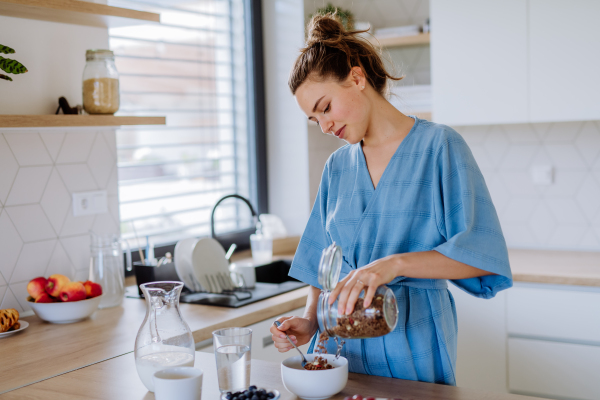 Young woman preparing a muesli for breakfast in her kitchen, morning routine and healthy lifestyle concept.