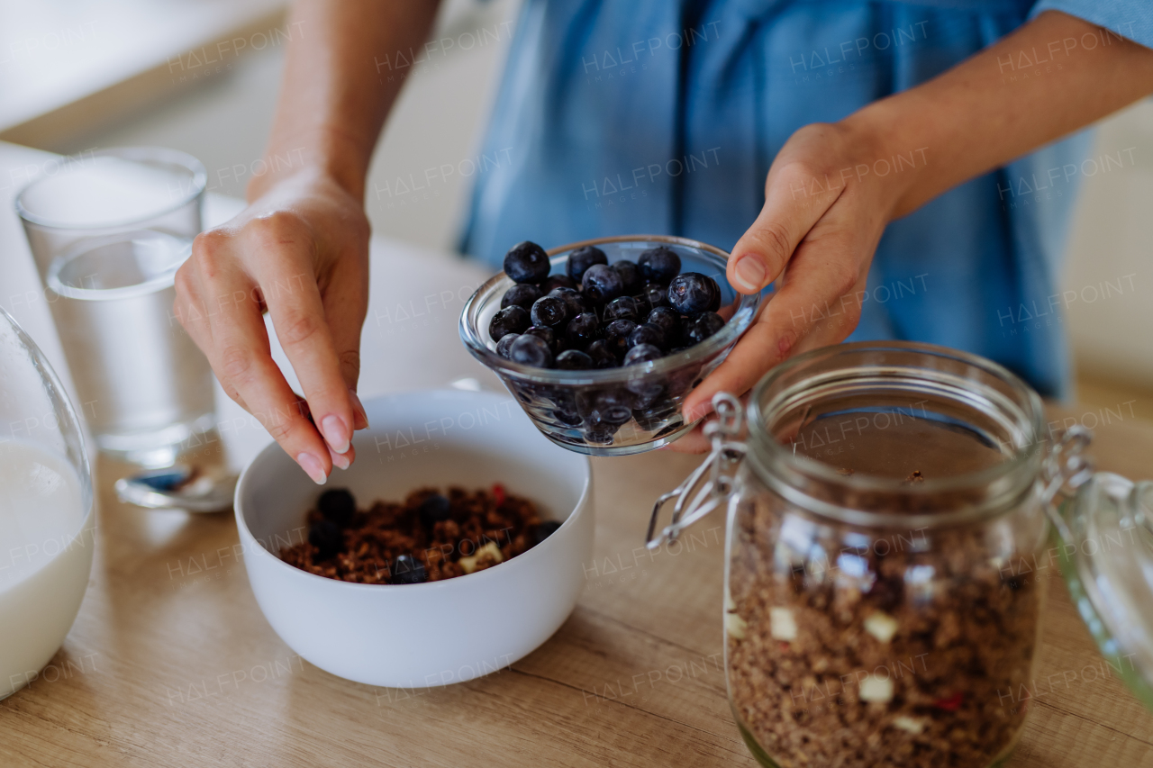 Close-up of young woman preparing a muesli for breakfast in her kitchen, morning routine and healthy lifestyle concept.