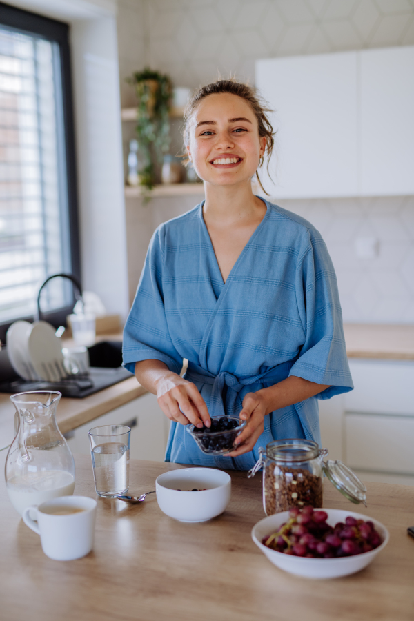 Young woman preparing a muesli for breakfast in her kitchen, morning routine and healthy lifestyle concept.