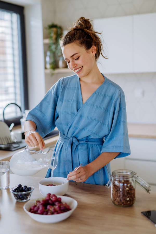 Young woman preparing a muesli for breakfast in her kitchen, morning routine and healthy lifestyle concept.