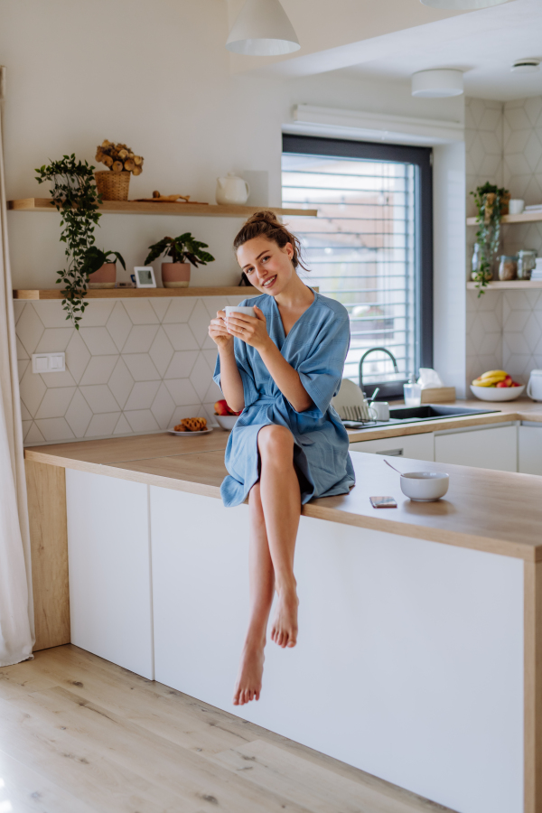 Young woman enjoying cup of coffee at morning, in a kitchen.