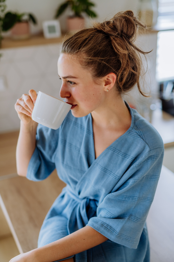 Young woman enjoying cup of coffee at morning, in a kitchen.