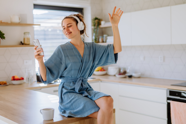 Young woman enjoying cup of coffee and listening music at morning, in a kitchen.