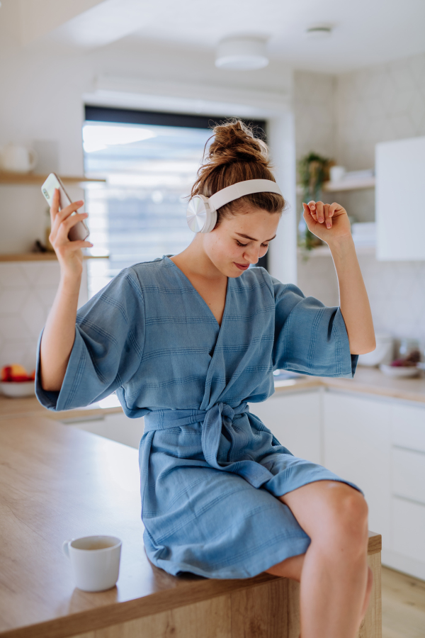 Young woman enjoying cup of coffee and listening music at morning, in a kitchen.