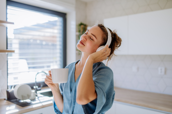 Young woman enjoying cup of coffee and listening music at morning, in a kitchen.