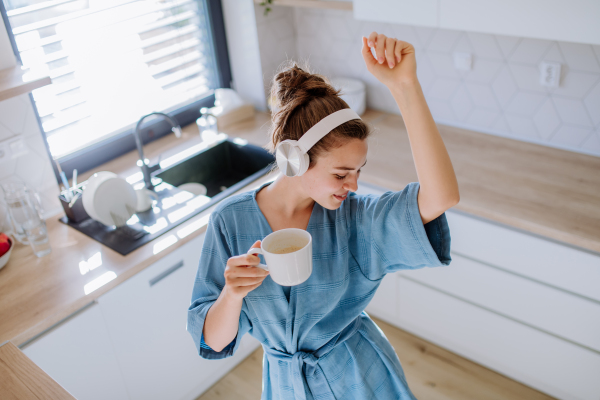 Young woman enjoying cup of coffee and listening music at morning, in a kitchen.