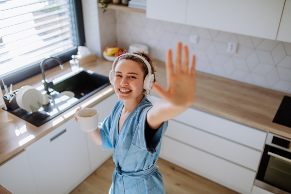 Young woman enjoying cup of coffee and listening music at morning, in a kitchen.