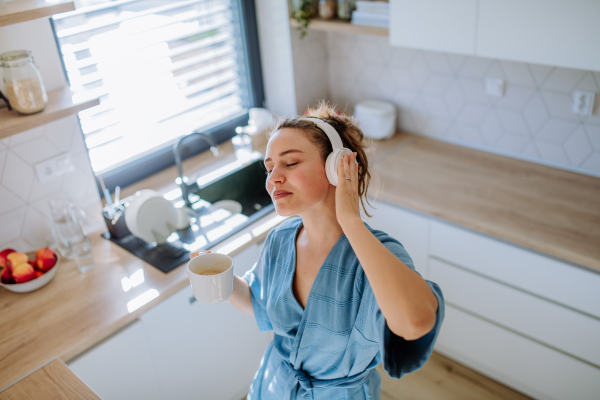 Young woman enjoying cup of coffee and listening music at morning, in a kitchen.