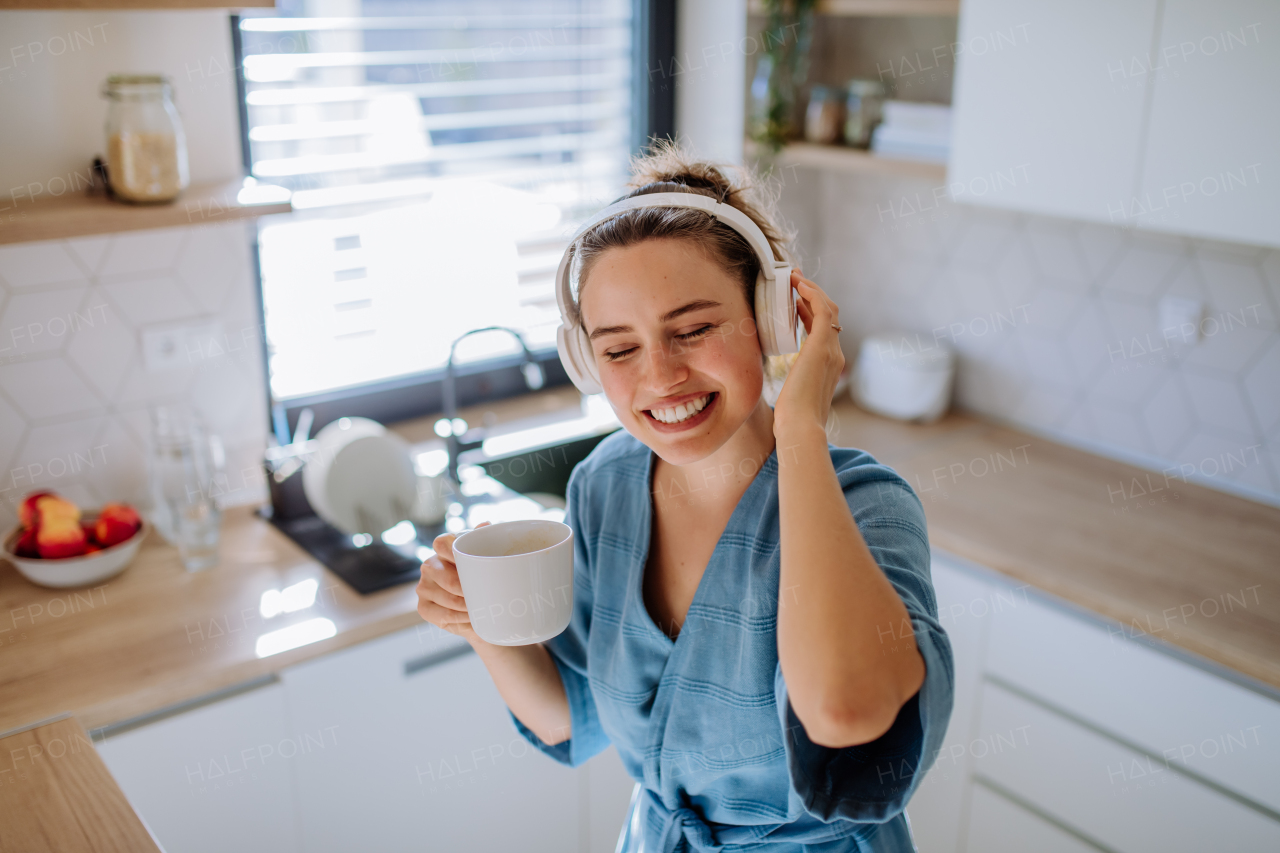 Young woman enjoying cup of coffee and listening music at morning, in a kitchen.