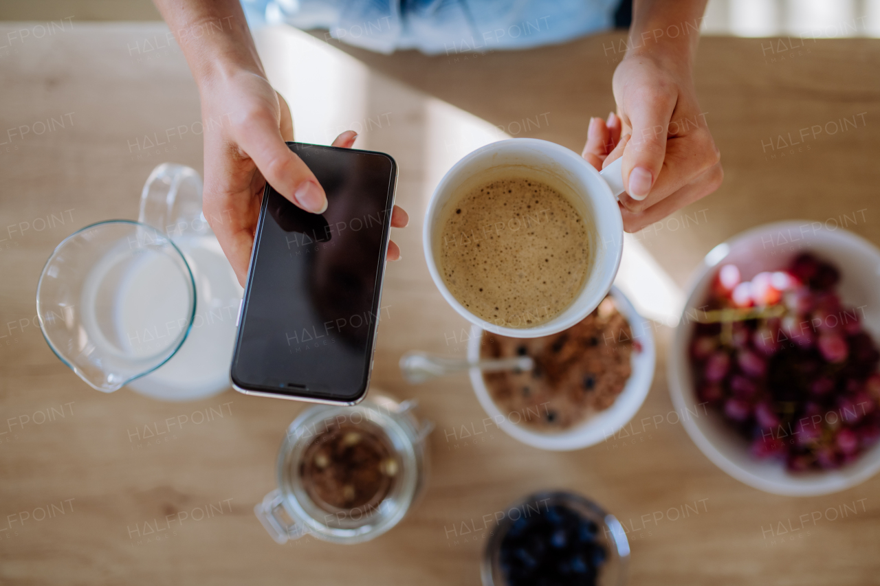 Top view of woman's hands with coffee and phone above breakfast.