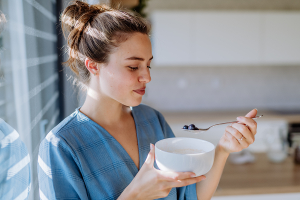 Young woman having a muesli for breakfast in her kitchen, morning routine and healthy lifestyle concept.