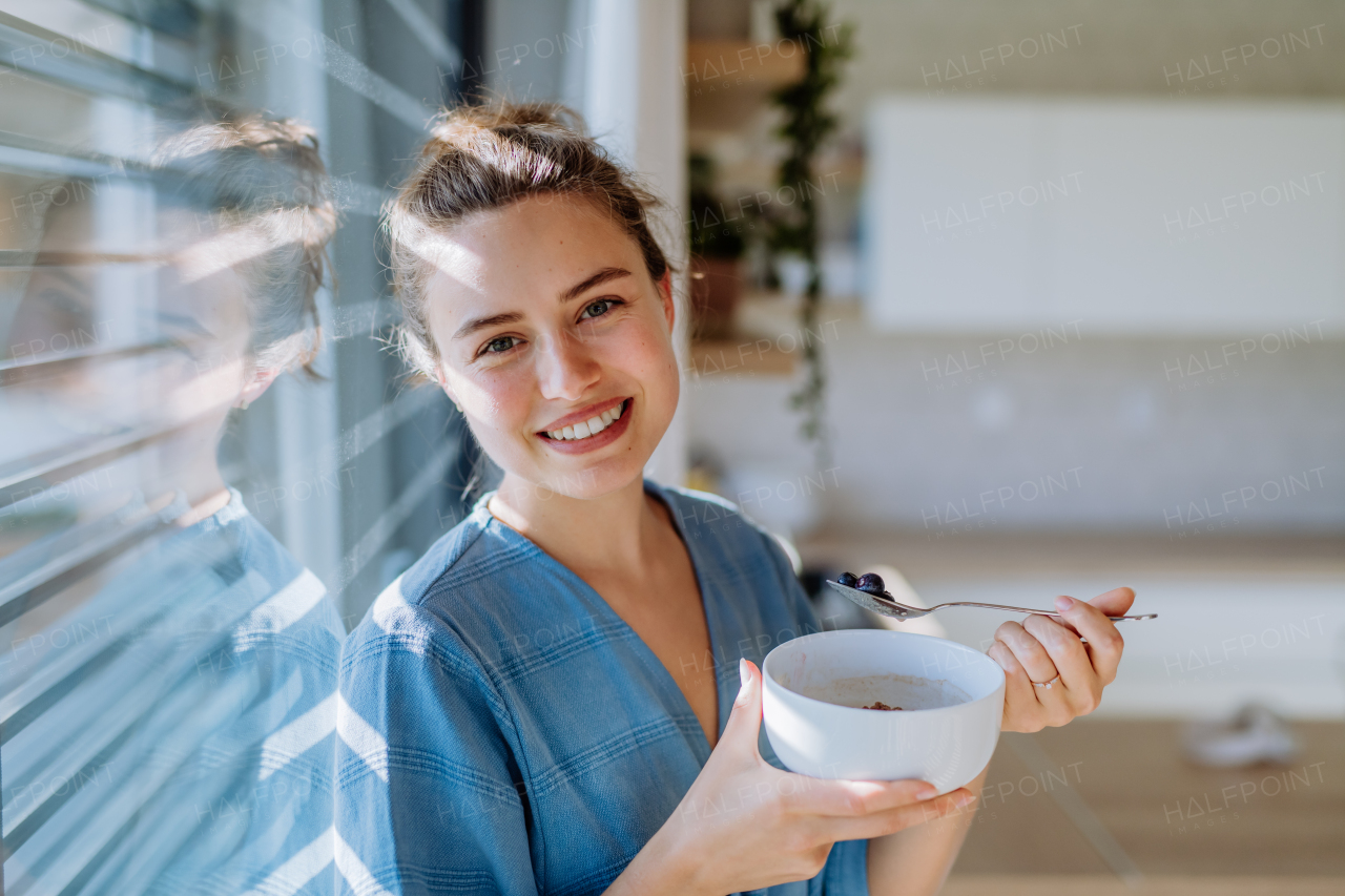 Young woman having a muesli for breakfast in her kitchen, morning routine and healthy lifestyle concept.