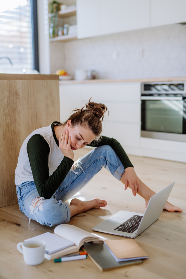 Young woman sitting with laptop and cup of coffee in her kitchen.