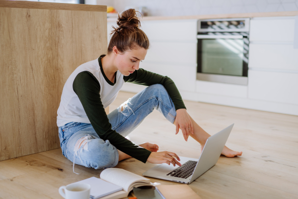 Young woman sitting with laptop and cup of coffee in her kitchen.