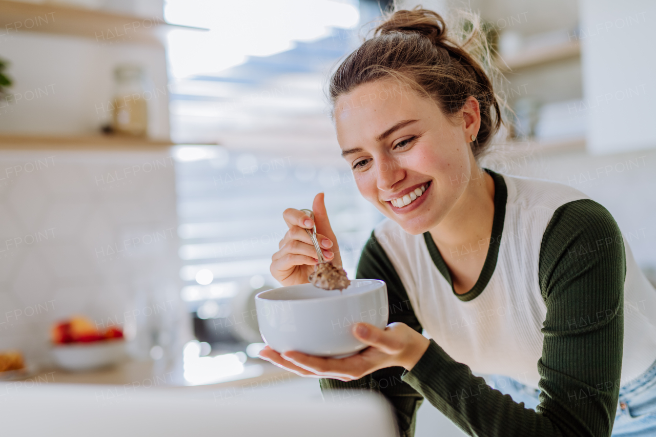 Young woman having a muesli for breakfast in her kitchen, morning routine and healthy lifestyle concept.