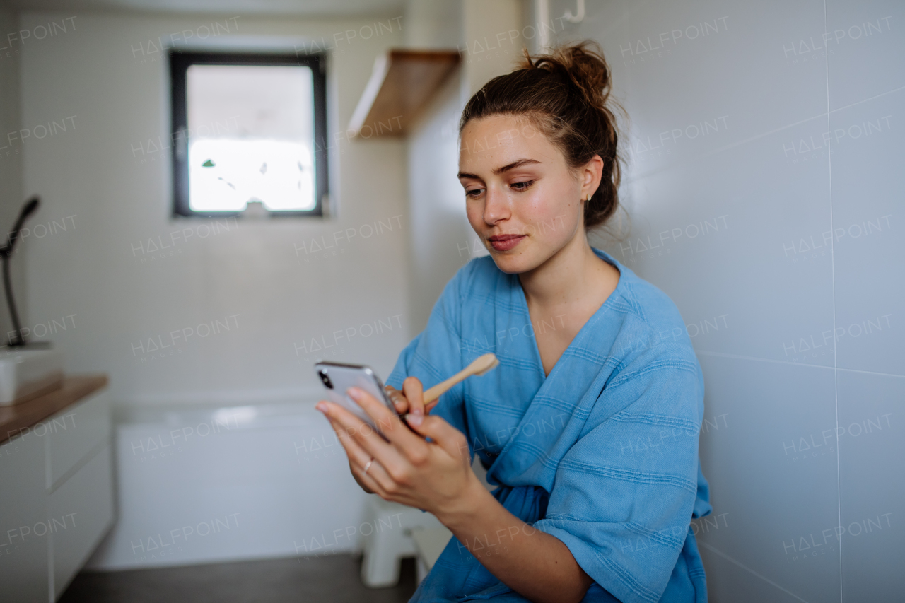 Young woman brushing teeth and scrolling her smartphone, morning routine concept.