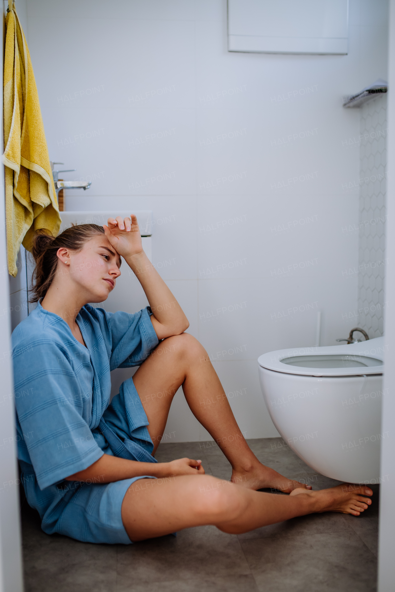 Young pregnant woman sitting on floor near toilet.