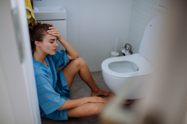 Young pregnant woman sitting on floor near toilet.