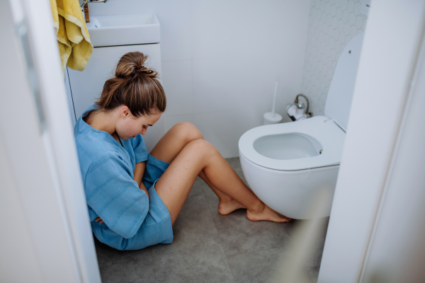 Young pregnant woman sitting on floor near toilet.