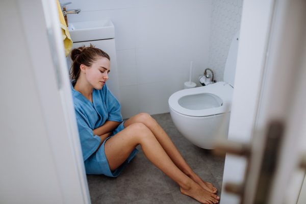 Young pregnant woman sitting on floor near toilet.