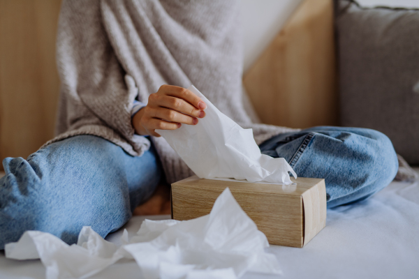 Sick woman sitting in bed, having a cold, close-up of the paper tissues.