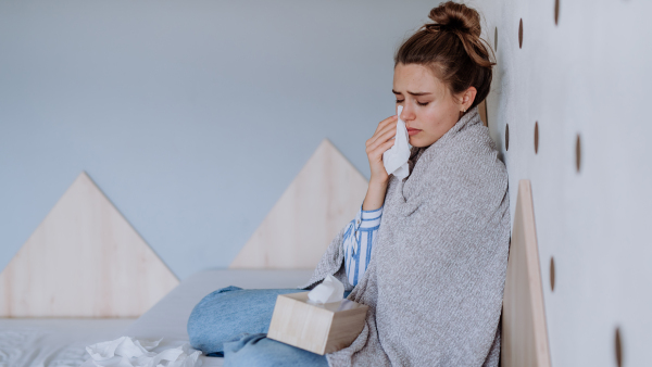 Sick woman sitting in a bed, having a cold.