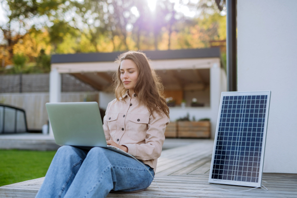 Young woman sitting on terrace, charging tablet trough the solar panel.