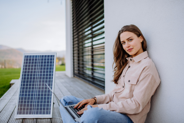 Young woman sitting on terrace, charging tablet trough the solar panel.