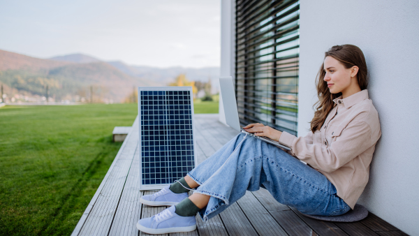 Young woman sitting on terrace, charging tablet trough the solar panel.