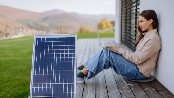 Young woman sitting on terrace, charging tablet trough the solar panel.