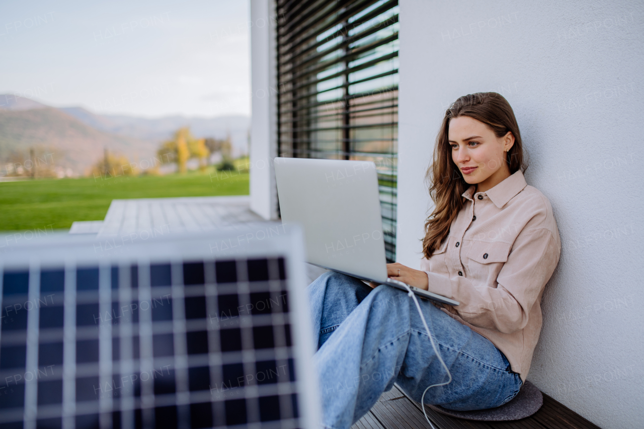 Young woman sitting on terrace, charging tablet trough the solar panel.