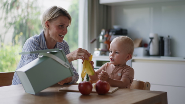 A mother teaching small baby to throw banana peel into organic waste bin. Kitchen compost bin. Sustainable living and future.