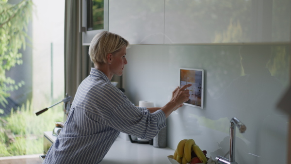 A beautiful woman adjusting smart home settings on touch screen device. Smart home technology for sustainable living.