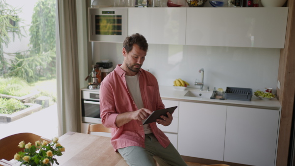 A handsome man adjusting smart home settings on touch screen device. Smart home technology for sustainable living.