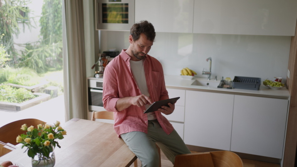 A handsome man adjusting smart home settings on touch screen device. Smart home technology for sustainable living.