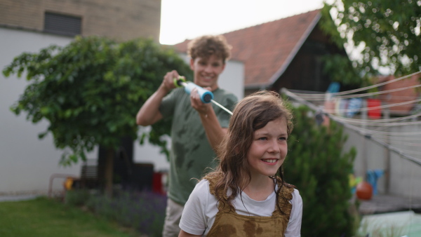 Siblings playing with water guns, foam water shooters during hot summer day. Children spending summer break outdoors on backyard.