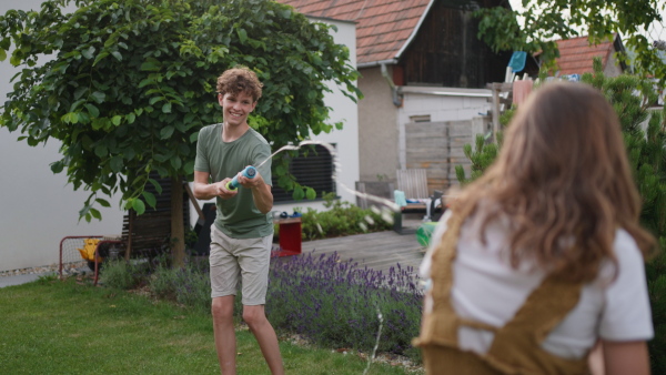 Siblings playing with water guns, foam water shooters during hot summer day. Children spending summer break outdoors on backyard.