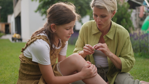 A mother treating her daughter's injury. Injured, bleeding knee after fall. Mom holding band aid and soothing crying girl.