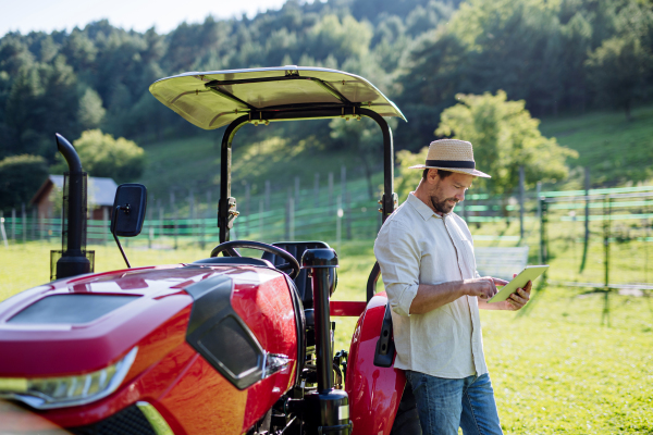 Farmer reading document in front of tractor on field. Grants, loans, funding opportunities for farmers. Agricultural support, subsidies.