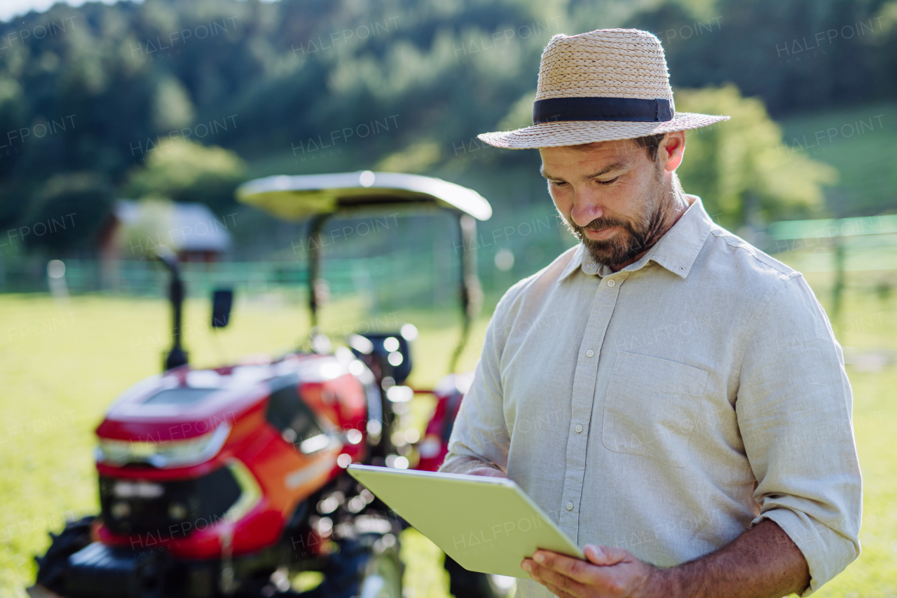 Farmer reading document in front of tractor on field. Grants, loans, funding opportunities for farmers. Agricultural support, subsidies.