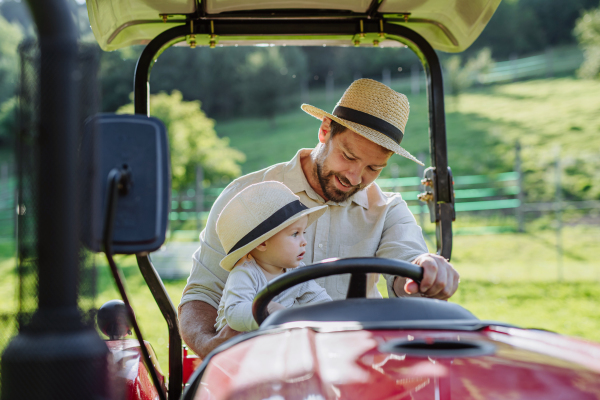 Farmer father riding tractor with his little baby son. Little baby growing up on family farm. Concept of multigenerational farming.